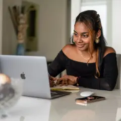 Giovane donna sorride mentre studia o lavora al computer, forse per insegnare inglese online.