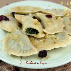 Pyszne pierogi ze szpinakiem i serem feta, okraszone cebulką i żurawiną, na talerzu.