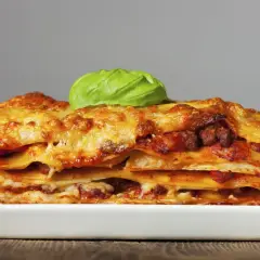 Una porción generosa de lasagna italiana, con capas de pasta, carne y queso derretido, coronada con una hoja de albahaca fresca.