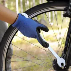 Ręka w niebieskiej rękawicy dokręca śrubę kluczem przy scentrowanym kole roweru.