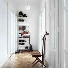 Helle Türen und ein schmaler Flur optisch breiter wirken lassen. Ein weißes Regal mit Hüten, Schuhen und einer Tasche steht im Flur.