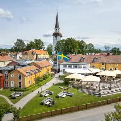 Mariefreds Värdshus med svensk flagga och kyrktorn. Uteservering med parasoller och sittgrupper i gräset.