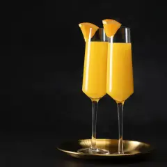Dwa kieliszki wypełnione złocistym płynem, ozdobione plasterkami pomarańczy. Idealny duet na brunch, klasyczny mimosa.