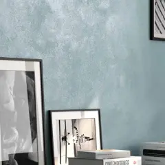 Parete con pittura effetto sabbiato azzurra, arricchita da quadri, vasi e libri. Ottime opinioni per questo stile.