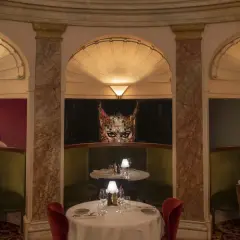Elegant bås med gröna sammetssoffor och röda stolar. Konstverk av en kvinna och en mask pryder väggarna. Perfekt för en lyxig operan lunch.