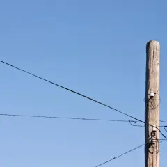 Drewniany słup z izolatorami, na którym widać światłowód na słupach. Linie energetyczne przecinają błękitne niebo.