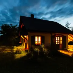Przytulny domek na cisowym wzgórzu, oświetlony ciepłym światłem z okien, na tle rozmytego, granatowego nieba.
