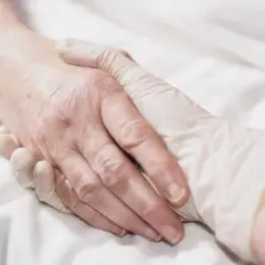 Dłoń w rękawiczce delikatnie obejmuje starszą dłoń. To obraz, który może wywołać refleksję nad tym, czym jest eutanazja.