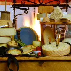 Un'abbondante tavola di formaggi, con una grande forma scavata che ricorda una fonduta di caprino, accompagnata da uva, fragole e pane tostato.