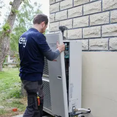 Un technicien installe une pompe à chaleur. La distance avec la maison du voisin est prise en compte pour le bruit.