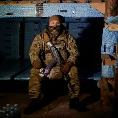 Żołnierz w mundurze, z karabinem, w ukryciu. Widać ukraińskie flagi, symbolizujące jego stopnie wojskowe Ukraina.