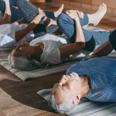 Grupa seniorów 60 plus ćwiczy gimnastykę na macie.