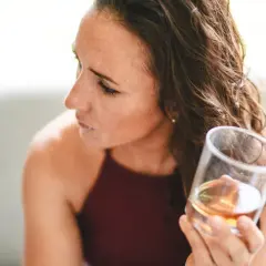 Kobieta zamyślona trzyma szklankę z bursztynowym płynem, zastanawiając się, jak ograniczyć alkohol.