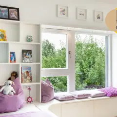 Gemütliches Kinderzimmer mit Bücherregalen, Spielzeug und einem Fensterplatz, der zum Entspannen einlädt. Ein schönes Beispiel für ein kinderfreundliches Zimmer, das auch ohne Fenster hell wirkt.