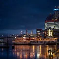Nocny widok na port z oświetlonymi statkami i nowoczesnym budynkiem.