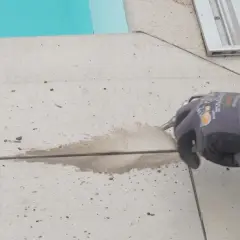 Arbeiter erneuert mit Sprühpistole die Silikonfugen auf gefliestem Boden neben einem Pool.
