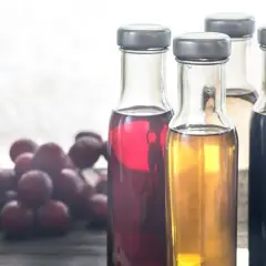 Flaschen mit verschiedenen Essigsorten, Äpfel und Trauben. Essigwasser gesund für den Körper.