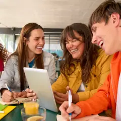 Uśmiechnięci studenci, którzy uczą się psychologii na studiach zaocznych, pracują razem przy stole, korzystając z laptopa i tabletu.