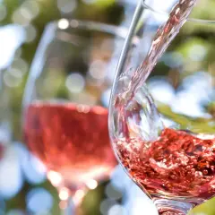 Vin rosé versé dans un verre, avec d'autres verres en arrière-plan flou.