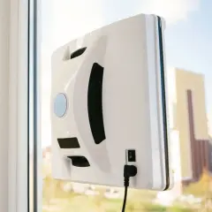 Biały robot do mycia okien przyczepiony do szyby. To urządzenie może być częścią rankingu robotów do mycia okien, ułatwiając czyszczenie.