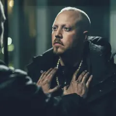 En dramatisk scen från en sebbe stakset film. Två män möts i mörkret, en med guldhalsband, den andra med händerna på hans bröst.
