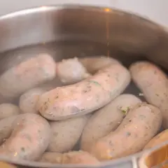 Kiełbasy gotują się w garnku. Idealna temperatura do parzenia kiełbasy to taka, by woda lekko wrzała, nie bulgotała.
