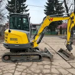 Żółta minikoparka Wacker Neuson z kabiną stoi na placu.