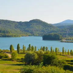 Vasta distesa azzurra del lago di Bilancino, circondata da dolci colline verdi e alberi rigogliosi sotto un cielo limpido.