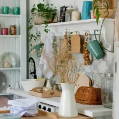A cozy granny chic kitchen with shelves full of colorful mugs, plates, and jars. A bouquet of dried flowers adds a rustic touch.