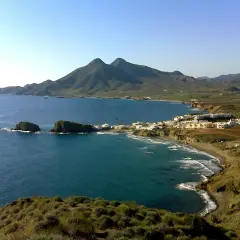 Vista panorámica de la cala del Toro, con sus aguas turquesas, rocas emergiendo y un pueblo blanco al fondo, bajo montañas verdes.
