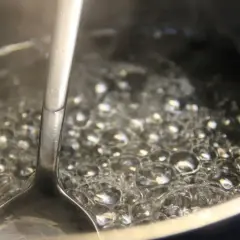 Metalowa łyżka zanurzona w bulgoczącej wodzie, tworzącej bąbelki. To początek pysznej przepalanki.