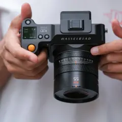 Dłonie trzymają aparat Hasselblad X2D 100C z obiektywem XCD 55mm. Widoczne detale aparatu i obiektywu.