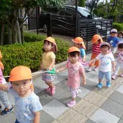 Un gruppo di bambini in Giappone, con cappellini arancioni, cammina in fila tenendo una corda.