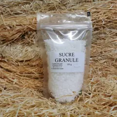 Un sachet de sucre granulé, 150g, est présenté sur un lit de copeaux de bois. Ce sucre granulé, c'est quoi ? C'est du sucre cristallisé.