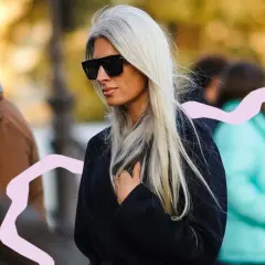 Mujer con pelo blanco largo y liso, gafas de sol oscuras y abrigo negro. La moda pelo blanco mujer es tendencia.