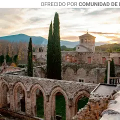Ruinas de antiguos monasterios cerca de Madrid, con arcos de piedra y cipreses altos bajo un cielo crepuscular.