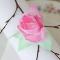 En rosa ros av blommor av kaffefilter, dekorerad med en kvist på en duk.