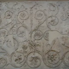Kamienna płaskorzeźba z bogatym ornamentem z natki, kwiatów i winogron. Widać też ptaka.