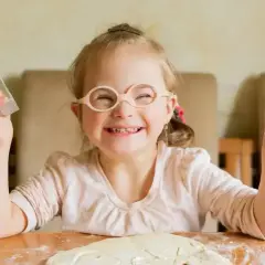 Uśmiechnięta dziewczynka z zespołem Downa w okularach trzyma foremki do ciastek, gotowa do pieczenia.