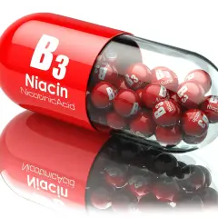 Czerwona kapsułka wypełniona małymi, błyszczącymi kulkami z napisem "B3 Niacin Nicotinic Acid". To witamina PP w pigułce.