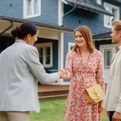 Un couple heureux serre la main d'une agente immobilière devant leur nouvelle maison. Ils ont réussi à vendre leur ancienne propriété et à garder leur prêt.