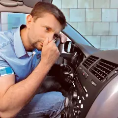 Mężczyzna w samochodzie czuje, że klimatyzacja w samochodzie nie chłodzi.