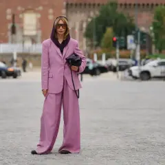 Kobieta w garniturze w kolorze mauve, z szerokimi nogawkami spodni, pozuje na tle miasta.