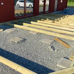 Grundarbete för att bygga altan på plattor. Träreglar läggs ut på grus och stenplattor, redo för altandäck.