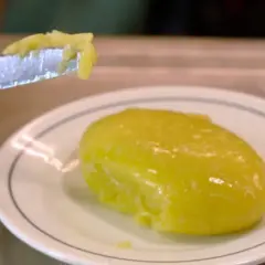 Un cuchillo recoge una porción de cremoso alioli casero, listo para untar sobre un plato blanco.