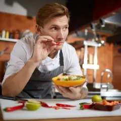 Koch probiert Chili, um scharf essen zu trainieren. Er hält eine Schüssel mit Salat und prüft die Schärfe.