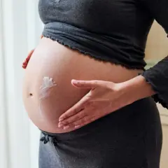 Gravid kvinna smörjer in sin mage med kräm för att motverka torr hud.