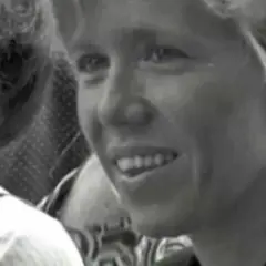 Uśmiechnięta żona Macrona w młodości, z jasnymi włosami, w otoczeniu innych osób.