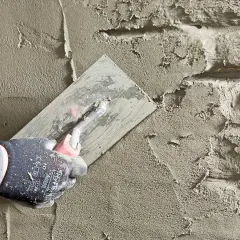 Hand mit Handschuh glättet Mörtel auf Bruchsteinmauer. Abdichten des Kellers mit Putz.