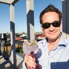 En man med solglasögon håller en rosa drink på en takterrass med utsikt över staden. En perfekt dag för en drink från arc blique by nobis.
